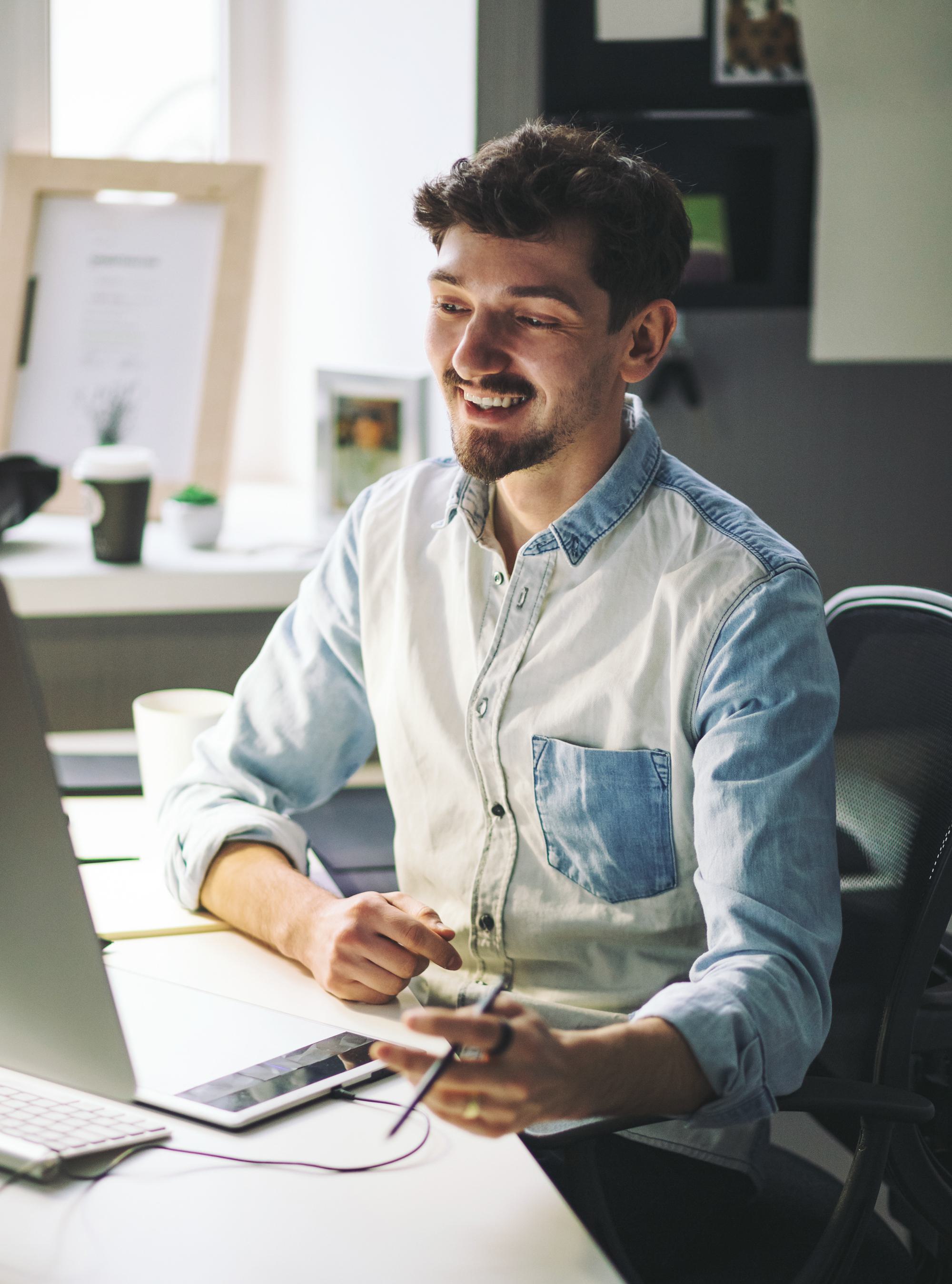 a smiling male employee working on a drawing tablet at his desk